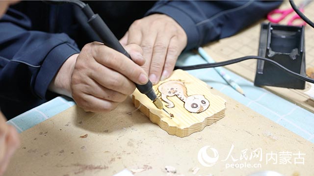 蘇殿政對(duì)朽木粘畫(huà)進(jìn)行燙畫(huà)工藝處理。孟佳澍攝